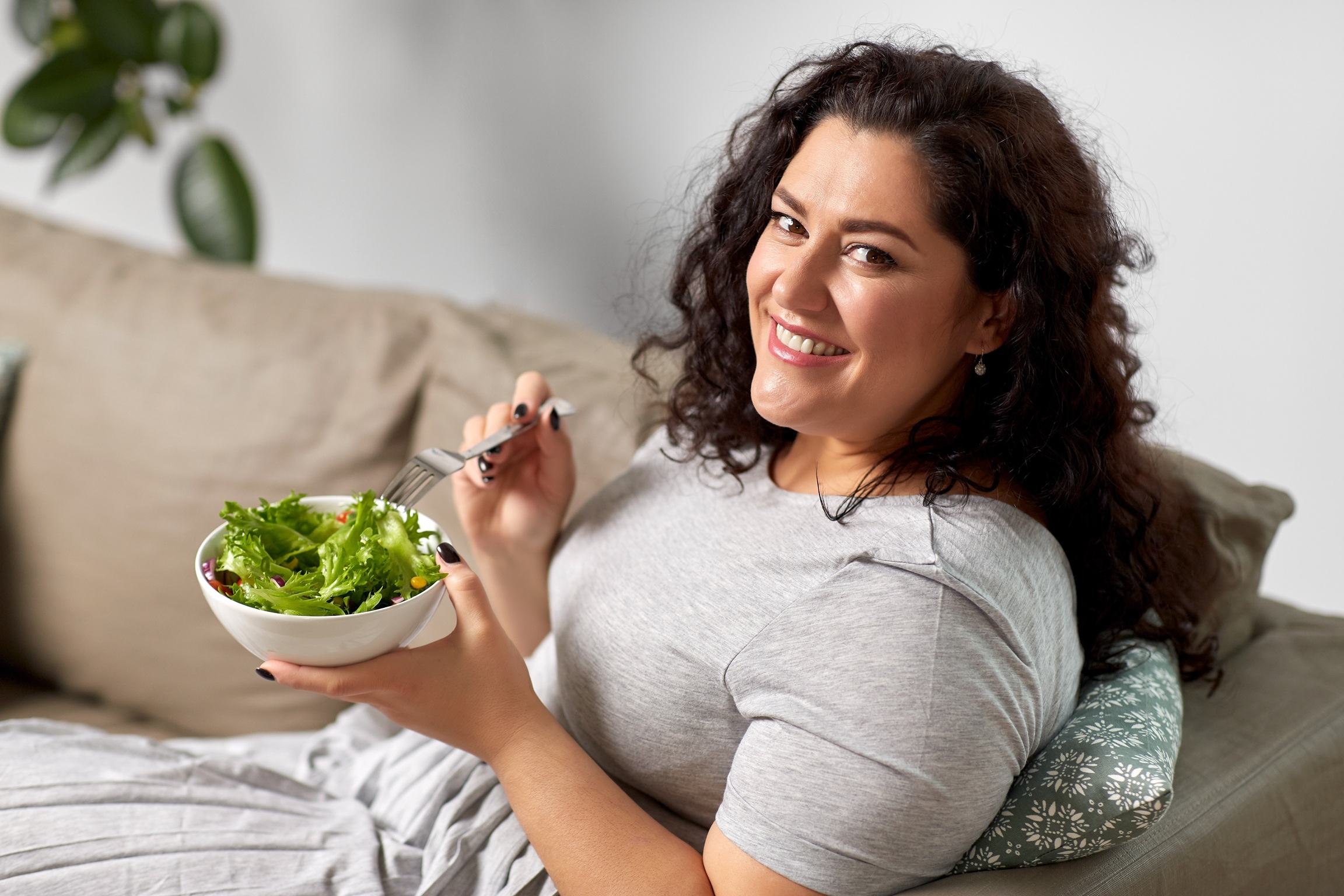 smiling young woman eating vegetable salad at home